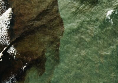 Aerial view of rocky shore meeting green ocean waves