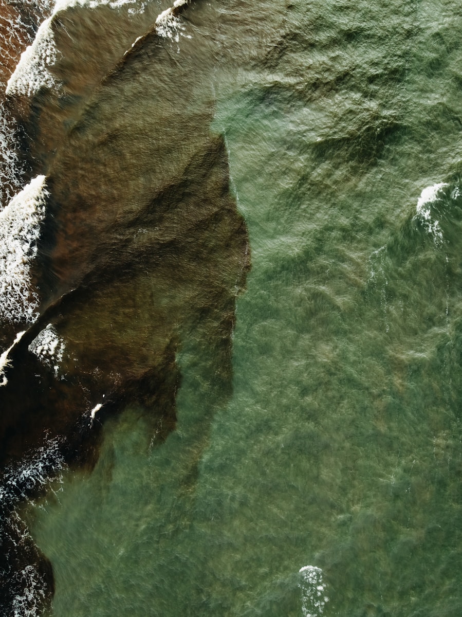 Aerial view of rocky shore meeting green ocean waves
